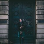 man in black jacket standing beside blue wooden door